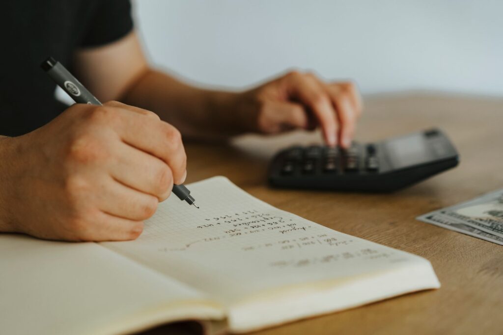 Person writing figures in a notebook while using a calculator