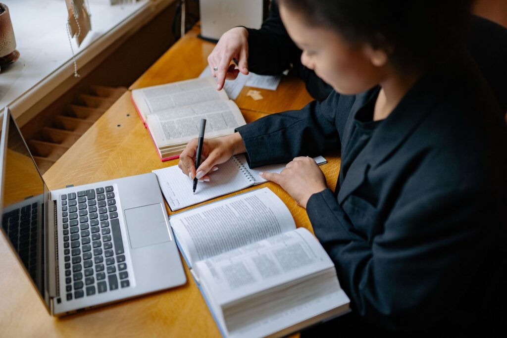Student writing notes by hand beside an open laptop and textbook