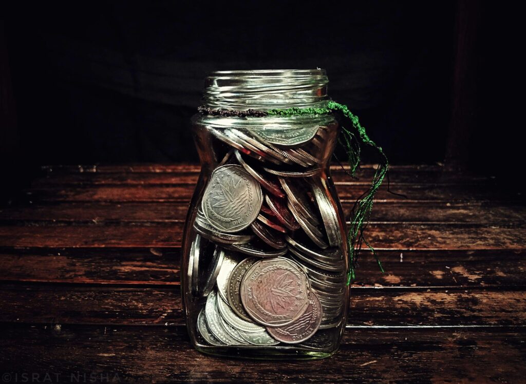 Glass jar filled with coins on a dark wooden surface