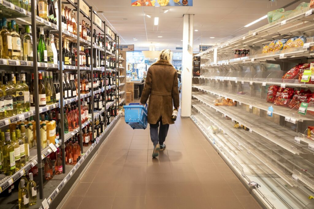 Shopper with a basket walking down a supermarket aisle